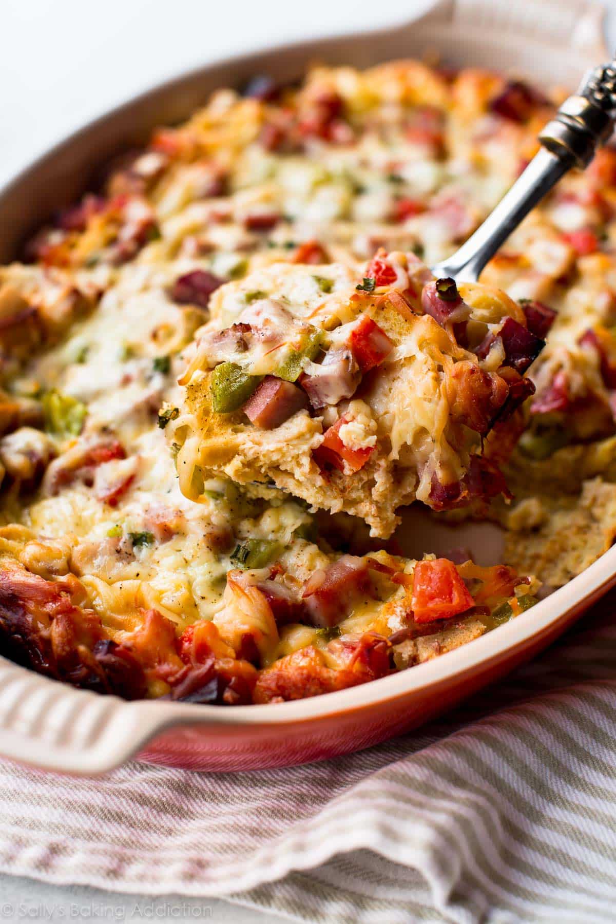 ham and cheese strata in a casserole dish with a serving spoon scooping a serving