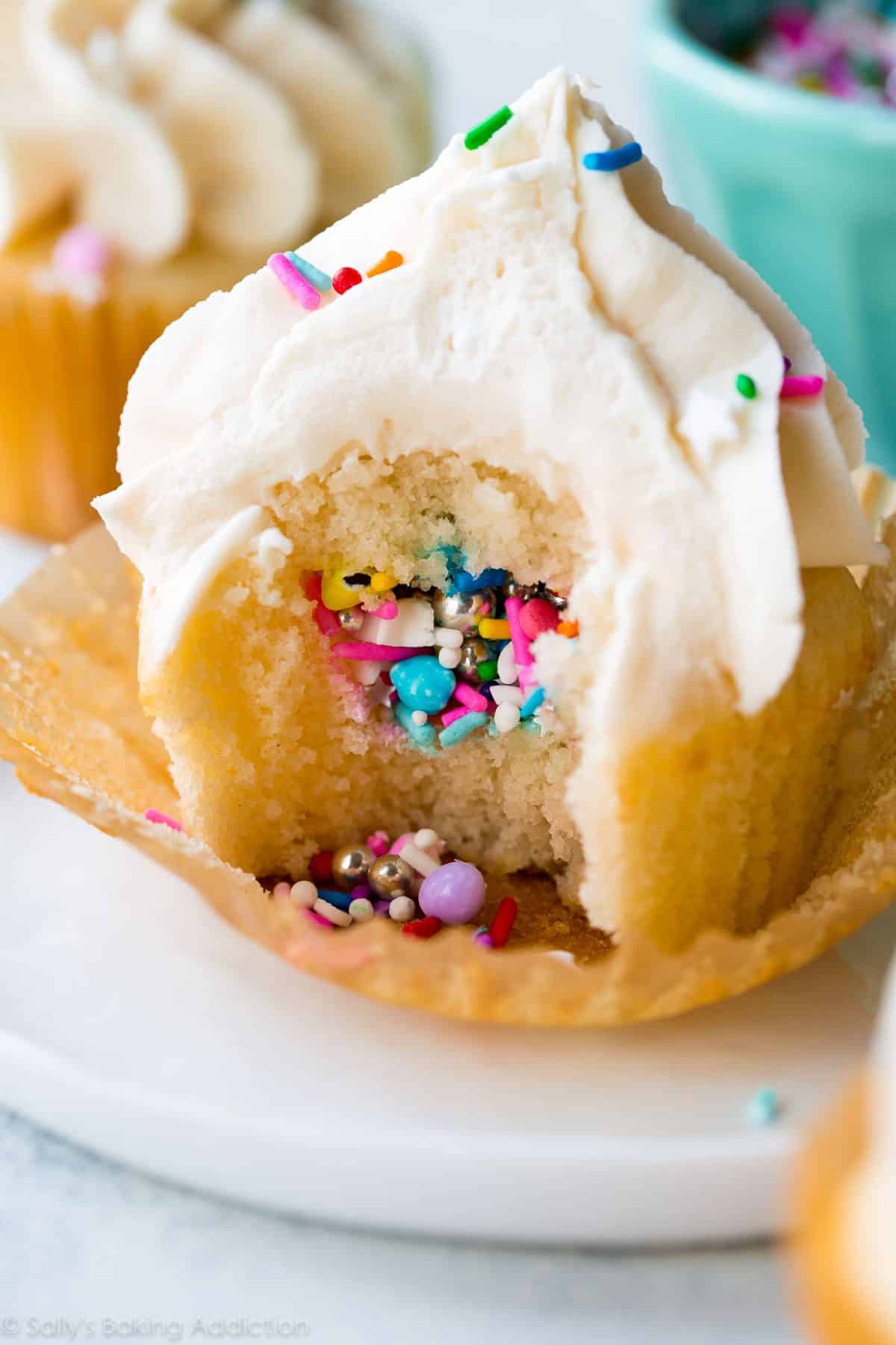 piñata cupcake on a white plate with a bite taken from it showing the sprinkles in the middle