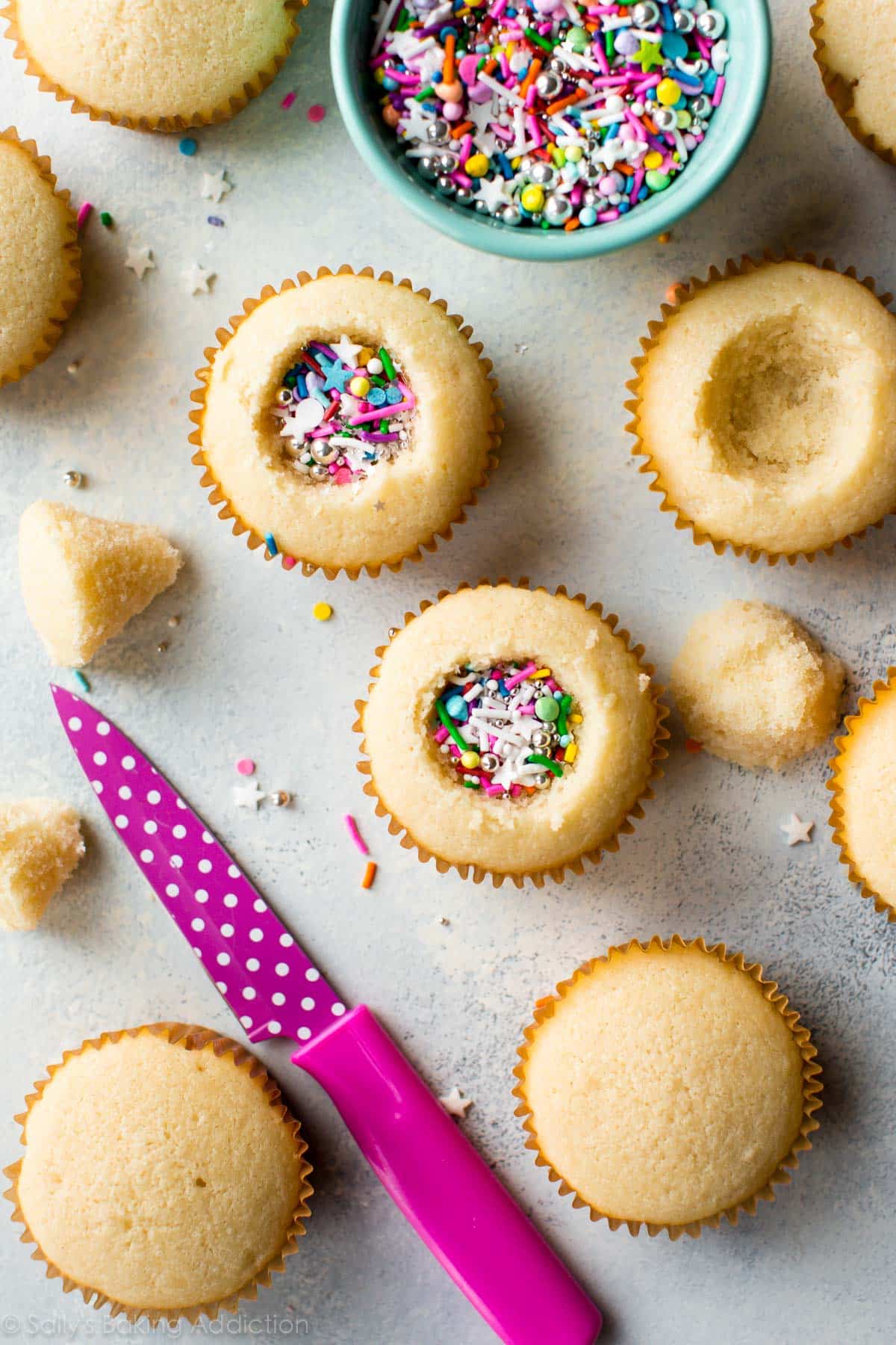 overhead image of vanilla cupcakes with the centers removed and filled with sprinkles