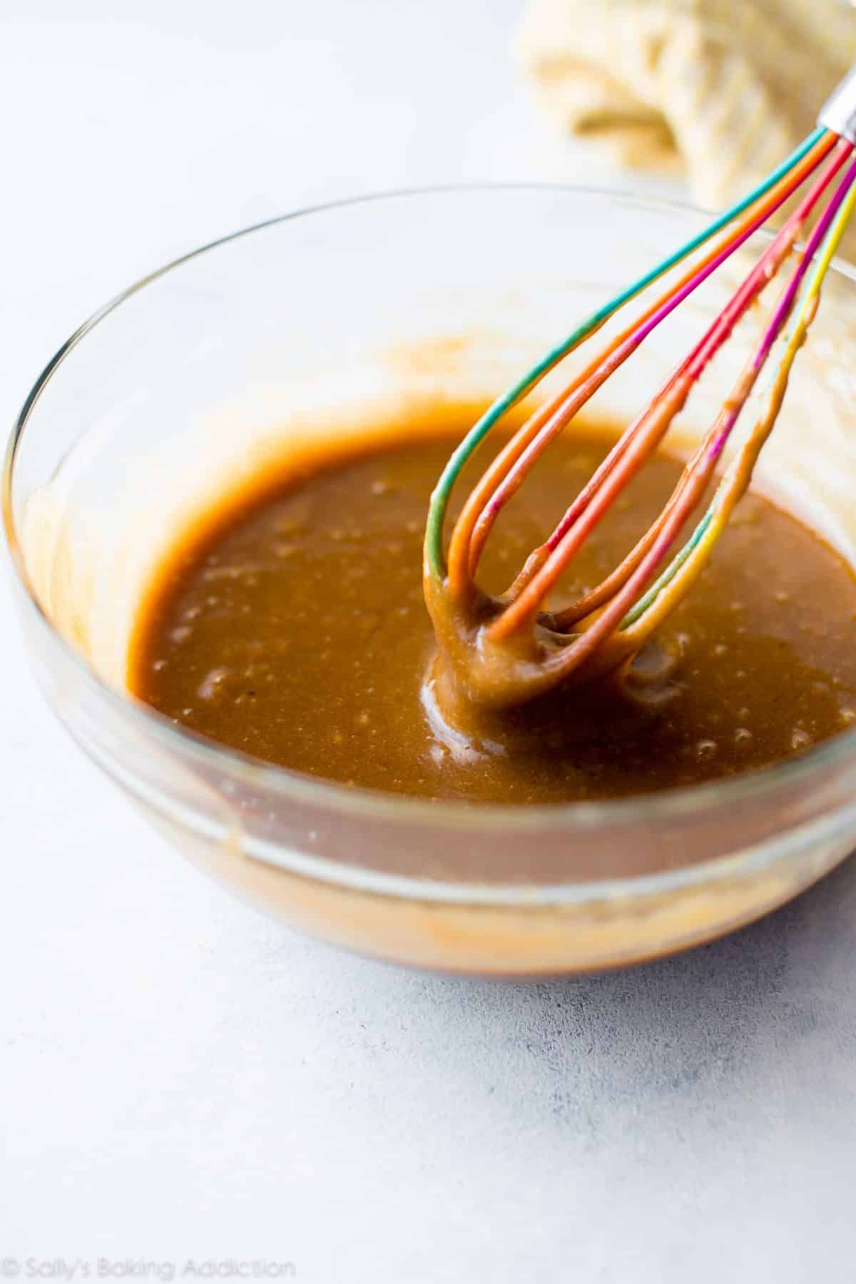 wet ingredients for peanut butter blondies in a glass bowl with a colorful whisk