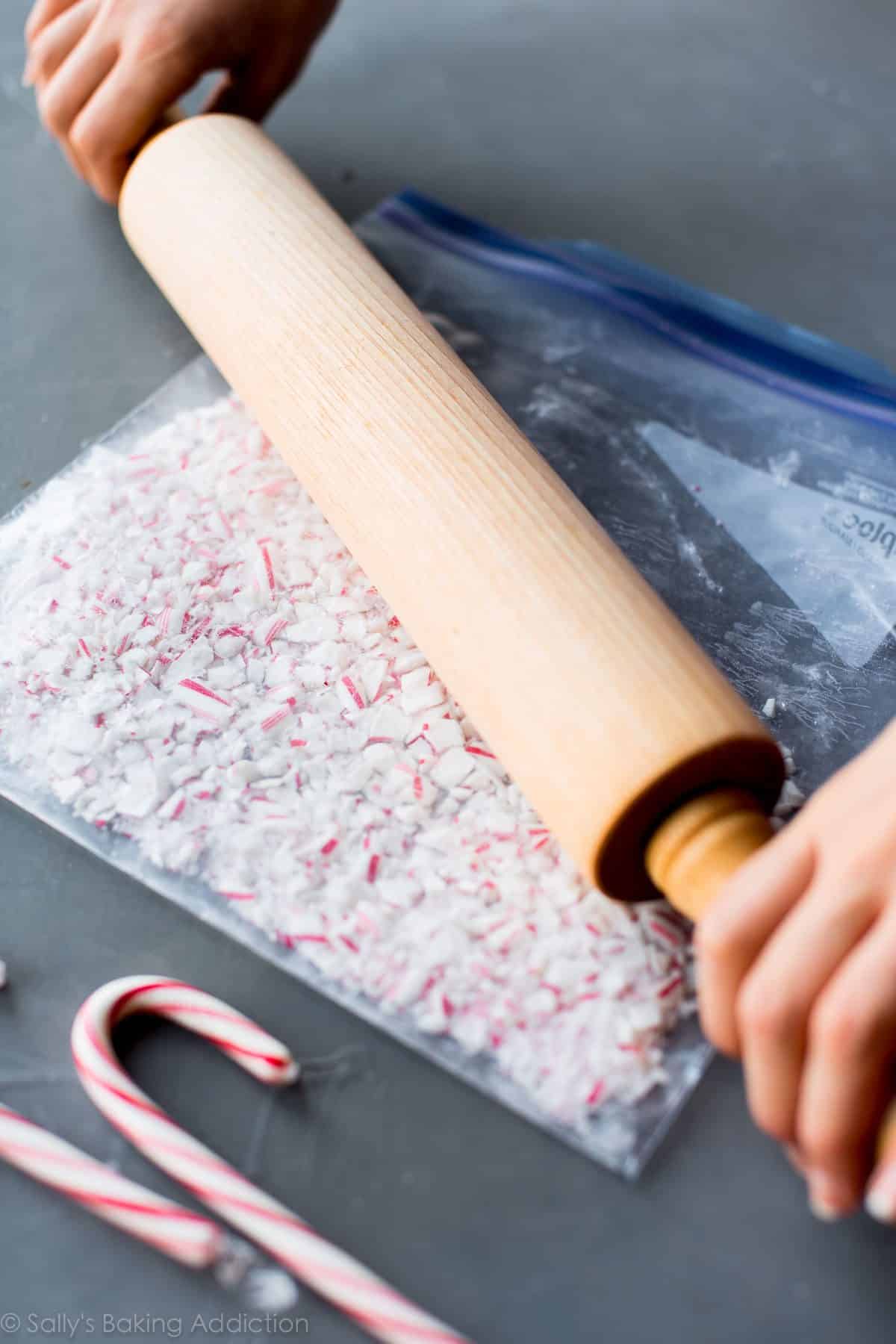 hands using a rolling pin to crush candy canes in a zip-top bag