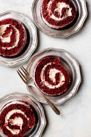 slices of red velvet cake roll on silver plates with a fork