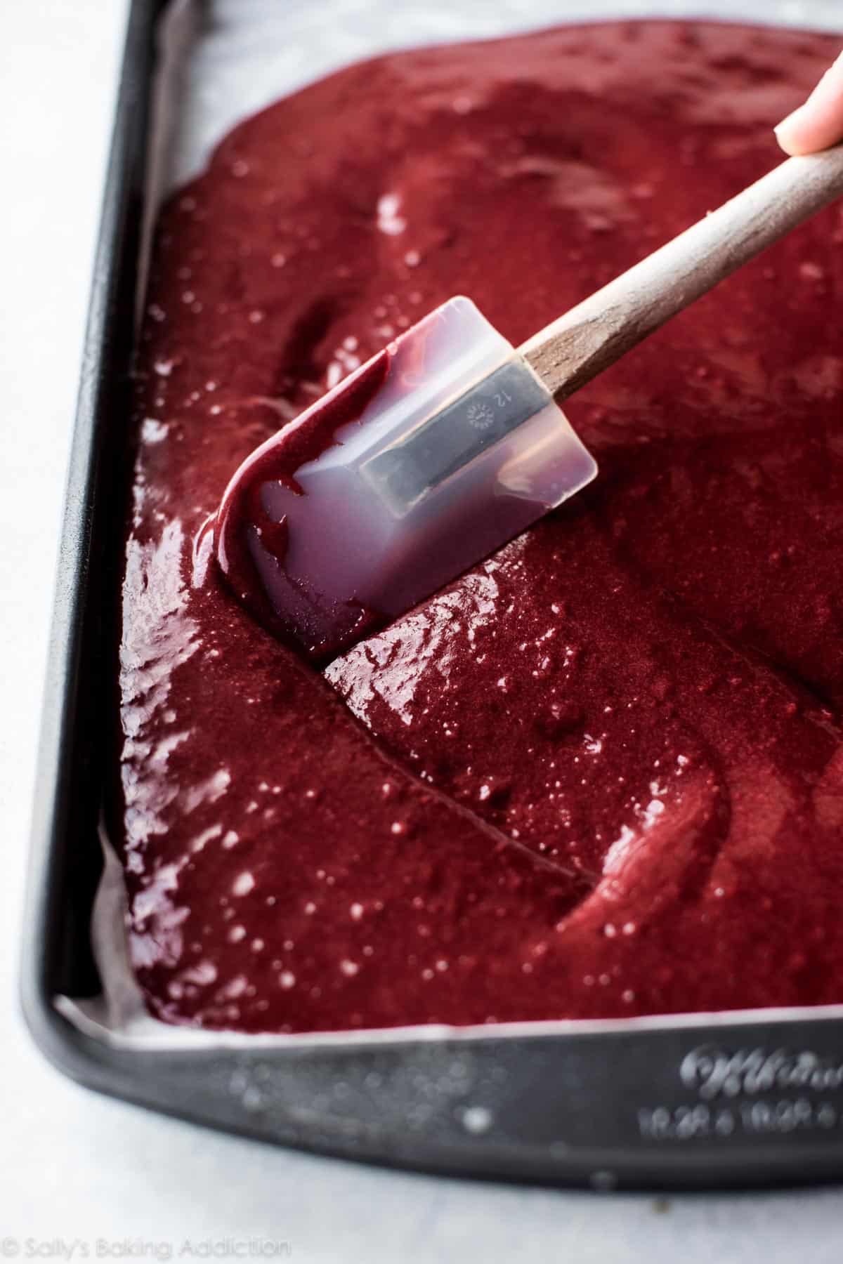 spreading red velvet cake batter into a jelly roll pan with a spatula