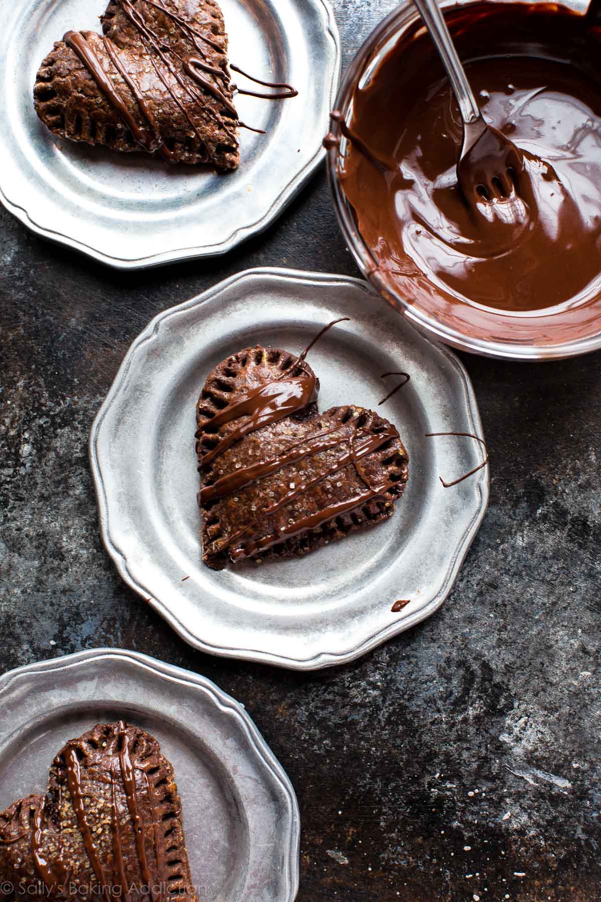 heart shaped chocolate hand pies on silver plates with a glass bowl of chocolate topping