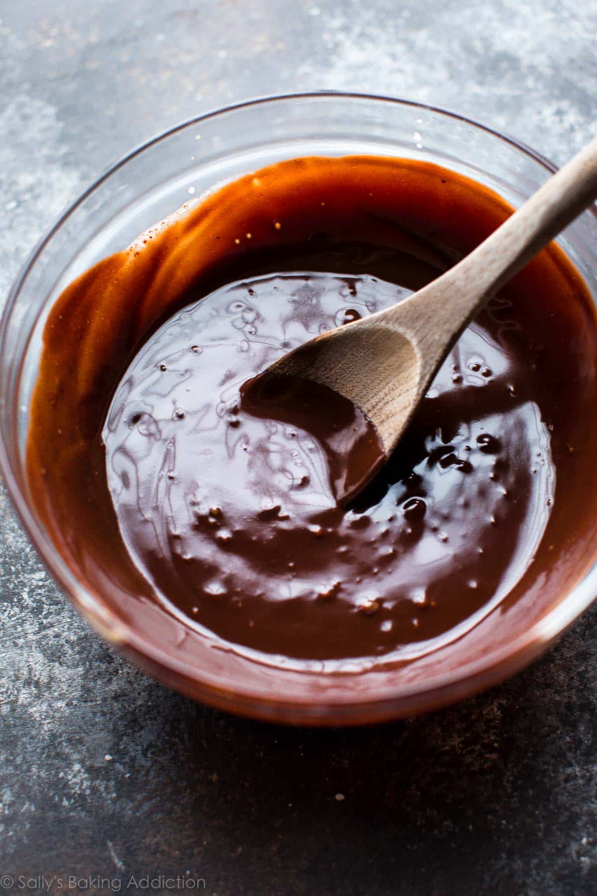 chocolate ganache in a glass bowl with a wood spoon