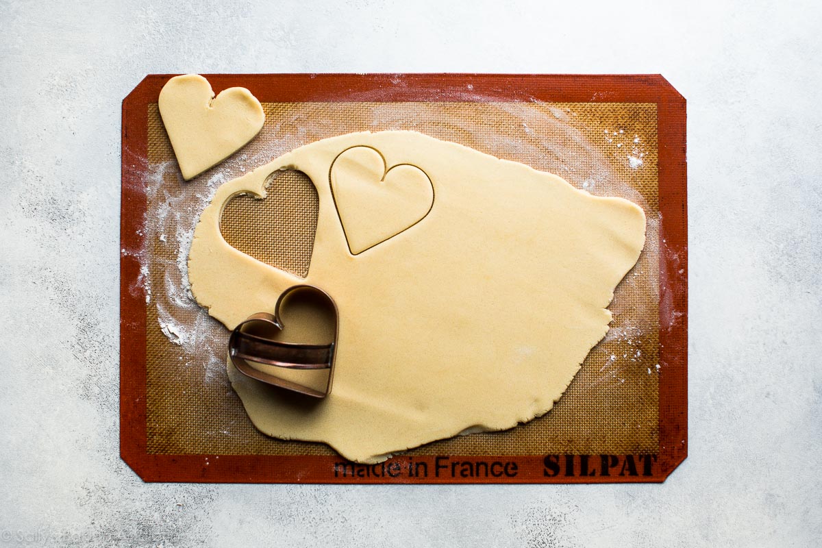 sugar cookie dough rolled out on silpat baking mat with heart cookie cutter