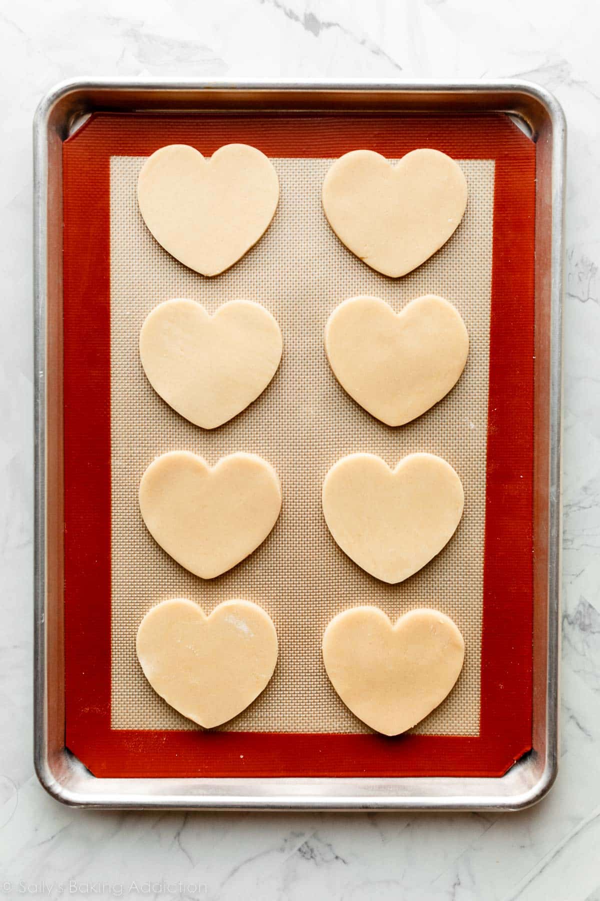 lined baking sheet with 8 heart-shaped sugar cookies on top before baking.
