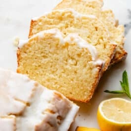 iced lemon pound cake loaf slices on marble board with lemons on the side.