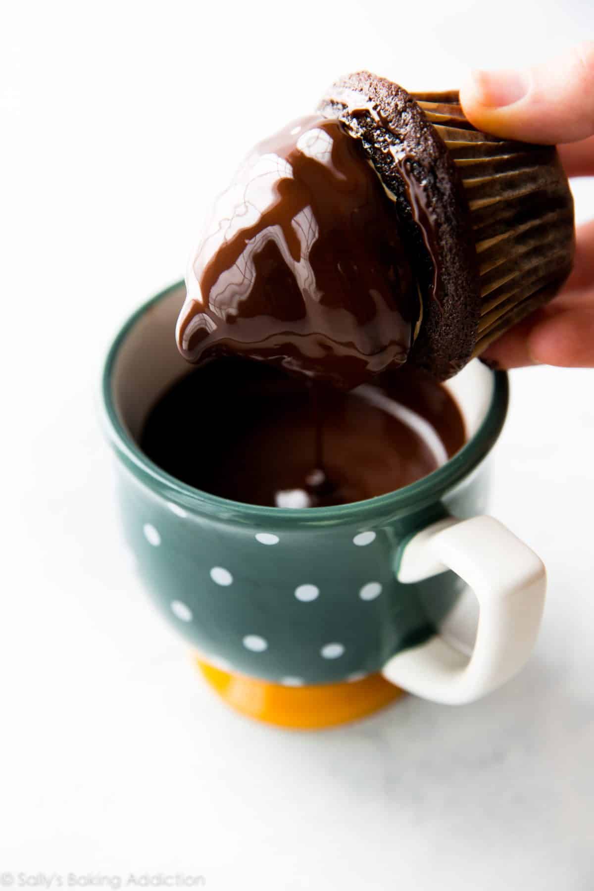 hands dunking a chocolate cupcake with peanut butter frosting into a mug of chocolate coating