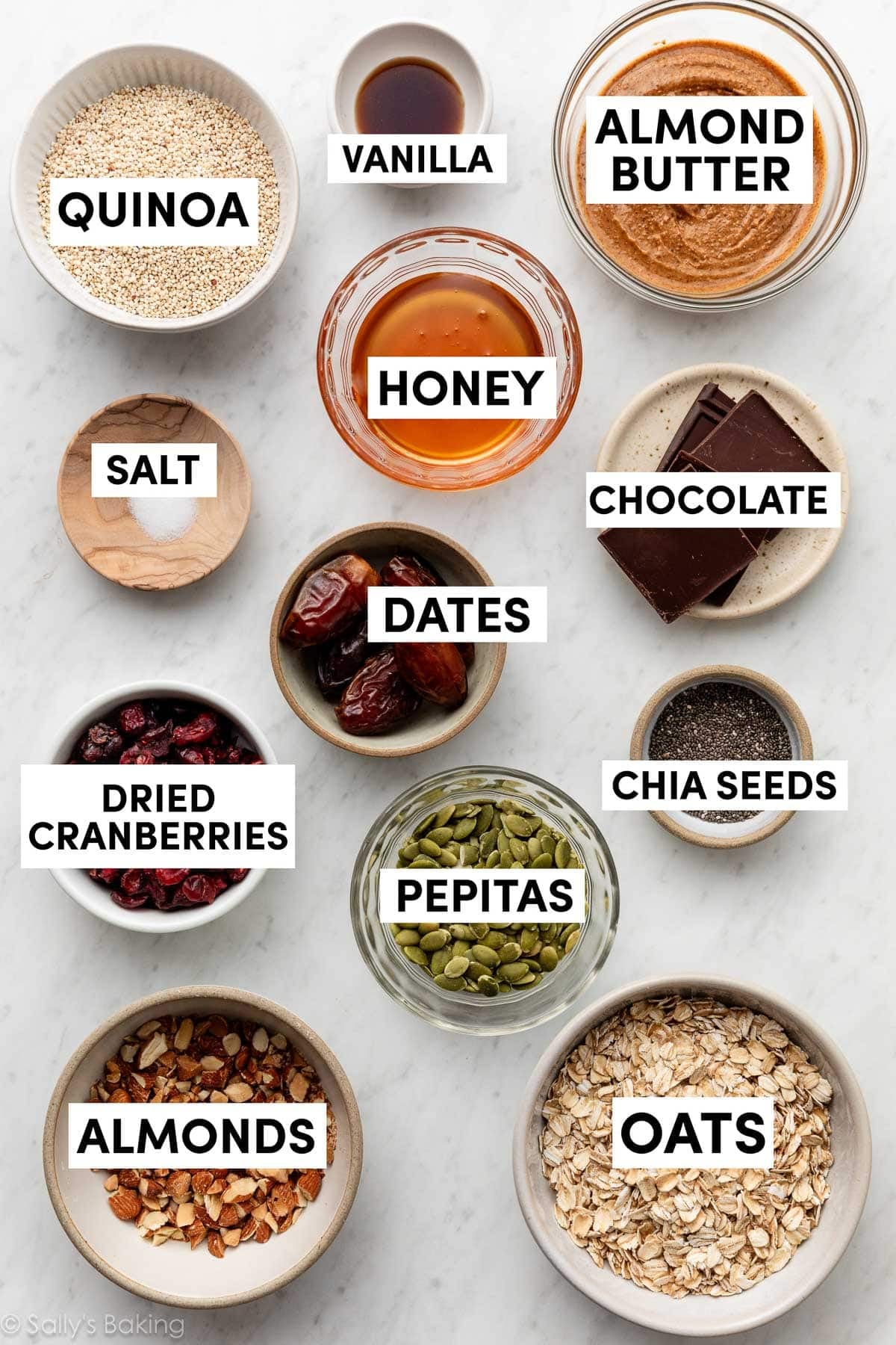 ingredients in bowls including almonds, pepitas, dried cranberries, dates, chocolate, and almond butter.