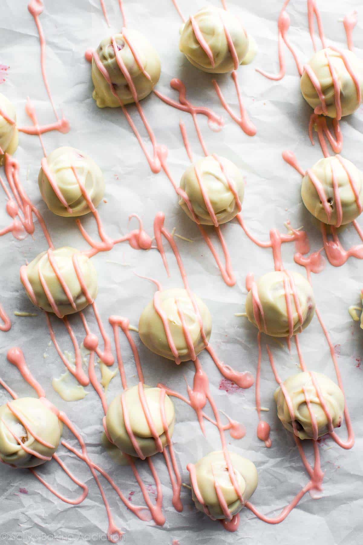 strawberry cheesecake truffles coated in white chocolate with a pink white chocolate drizzle on parchment paper