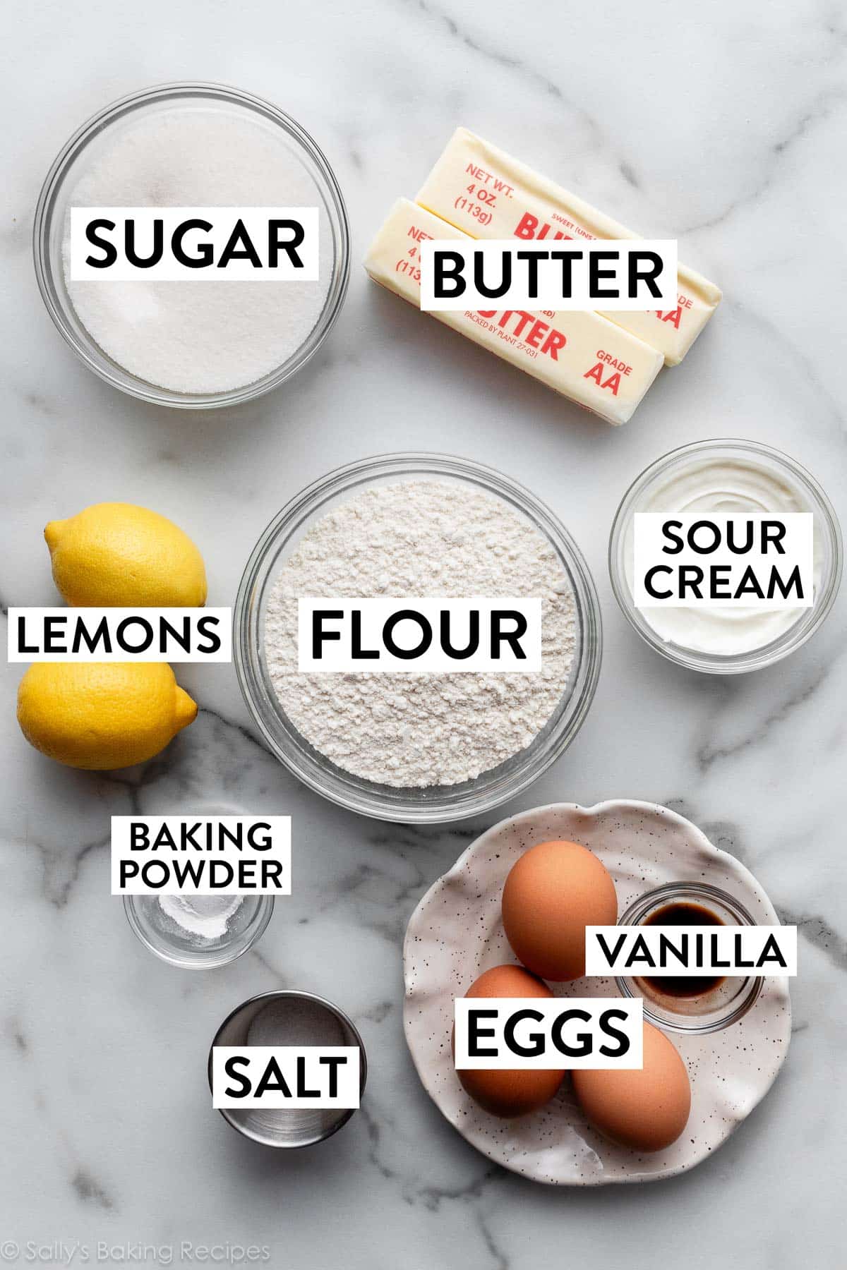 ingredients on marble counter including flour, butter, sour cream, eggs, vanilla, salt, and sugar.