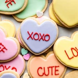 heart-shaped Valentine's Day cookies decorated in pastel royal icing and red writing to look like conversation heart candies.