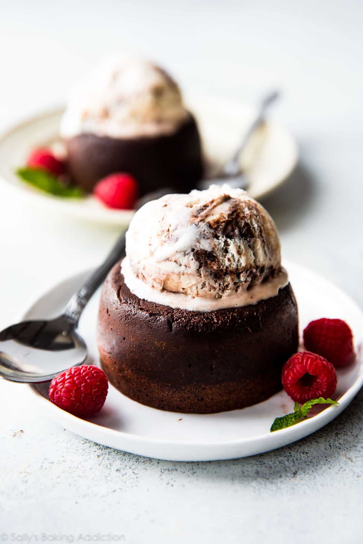 chocolate lava cakes topped with scoops of vanilla ice cream on a white plates with spoons