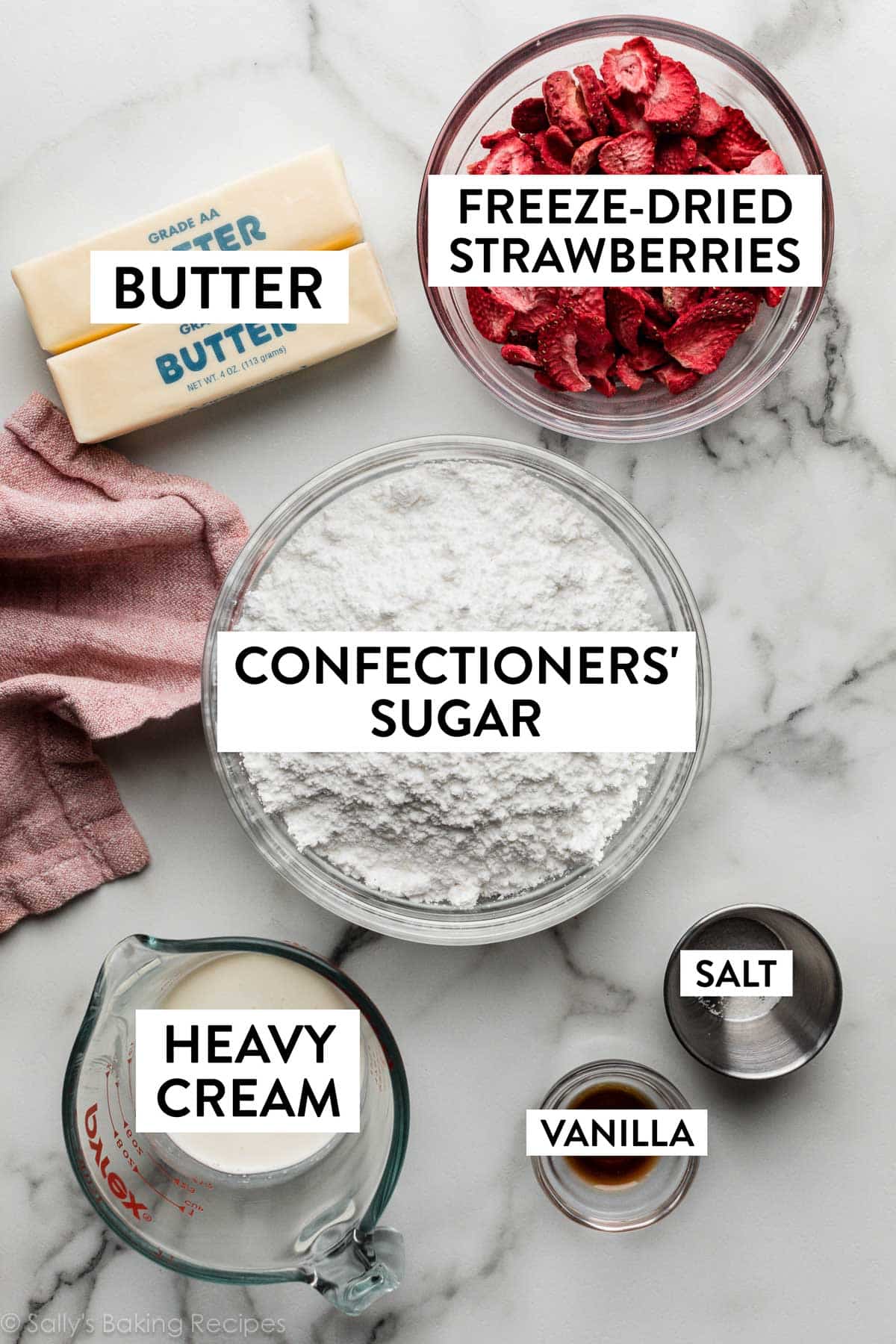 ingredients on marble counter including confectioners' sugar, freeze-dried strawberry slices, butter, and heavy cream.