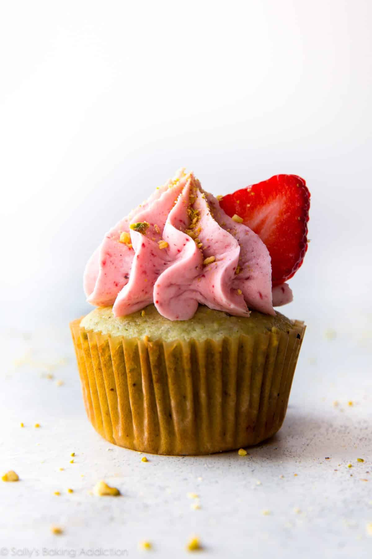 pistachio cupcake topped with strawberry frosting and a slice of strawberry