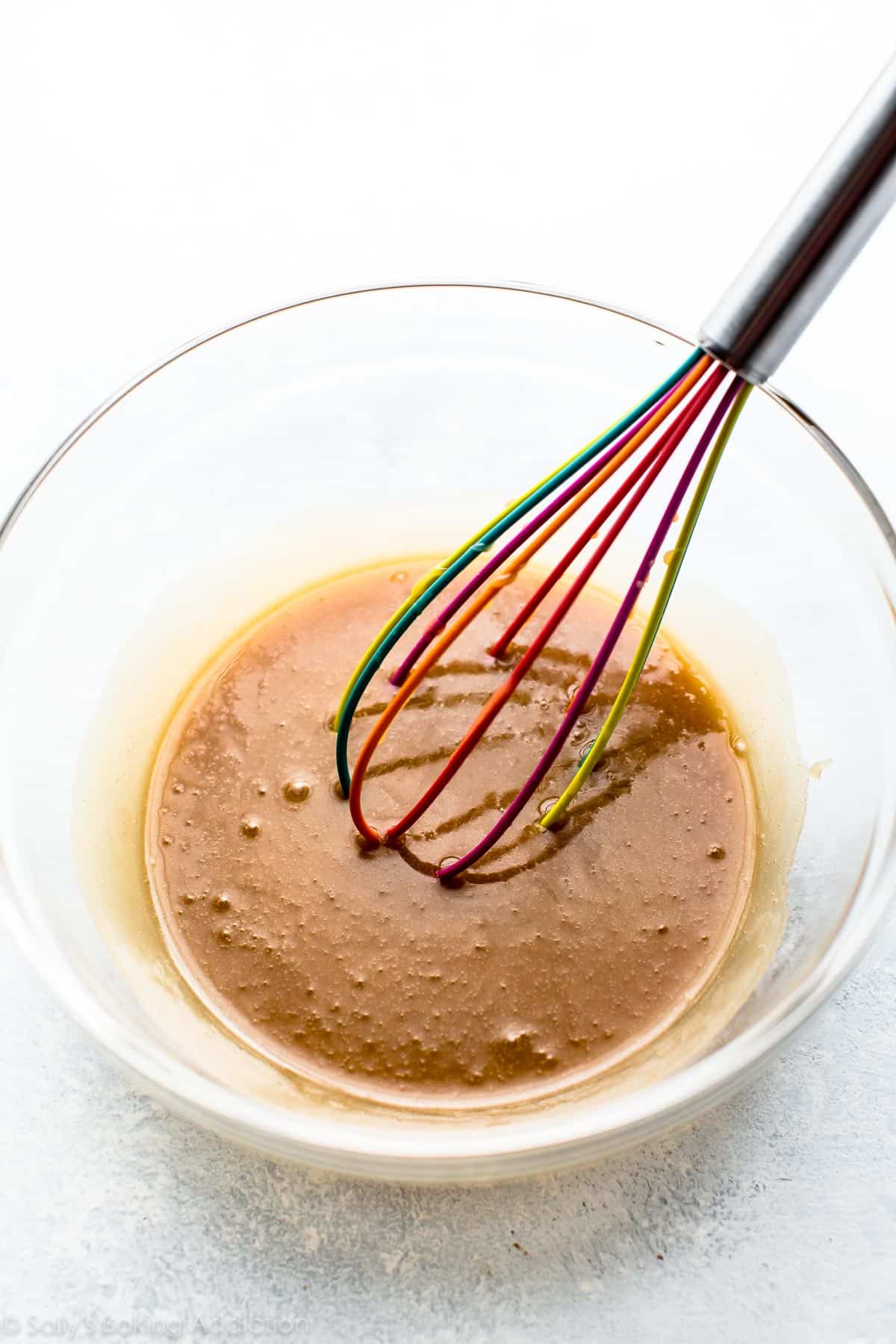 melted butter, sugar, cream, and salt in a glass bowl with a colorful whisk