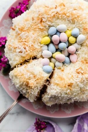 Easter cake decorated like a nest with a Bundt cake, coconut, and Easter chocolate egg candies on pink serving dish.