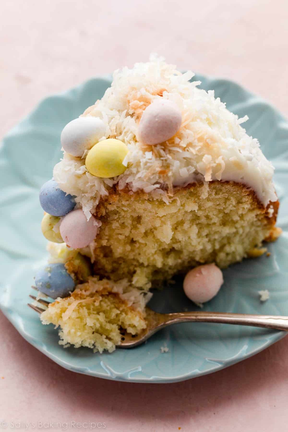 slice of coconut Bundt cake topped with cream cheese frosting and Easter chocolate egg candies on blue plate.