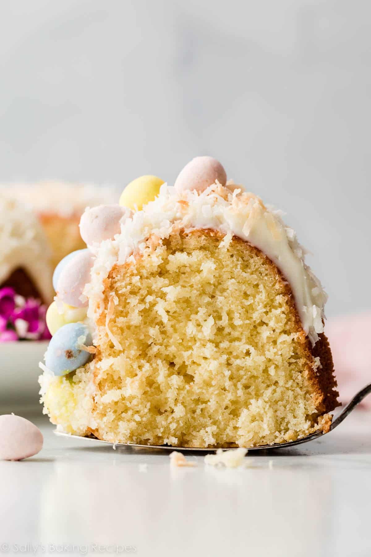 slice of coconut Bundt cake topped with cream cheese frosting and Easter chocolate egg candies.