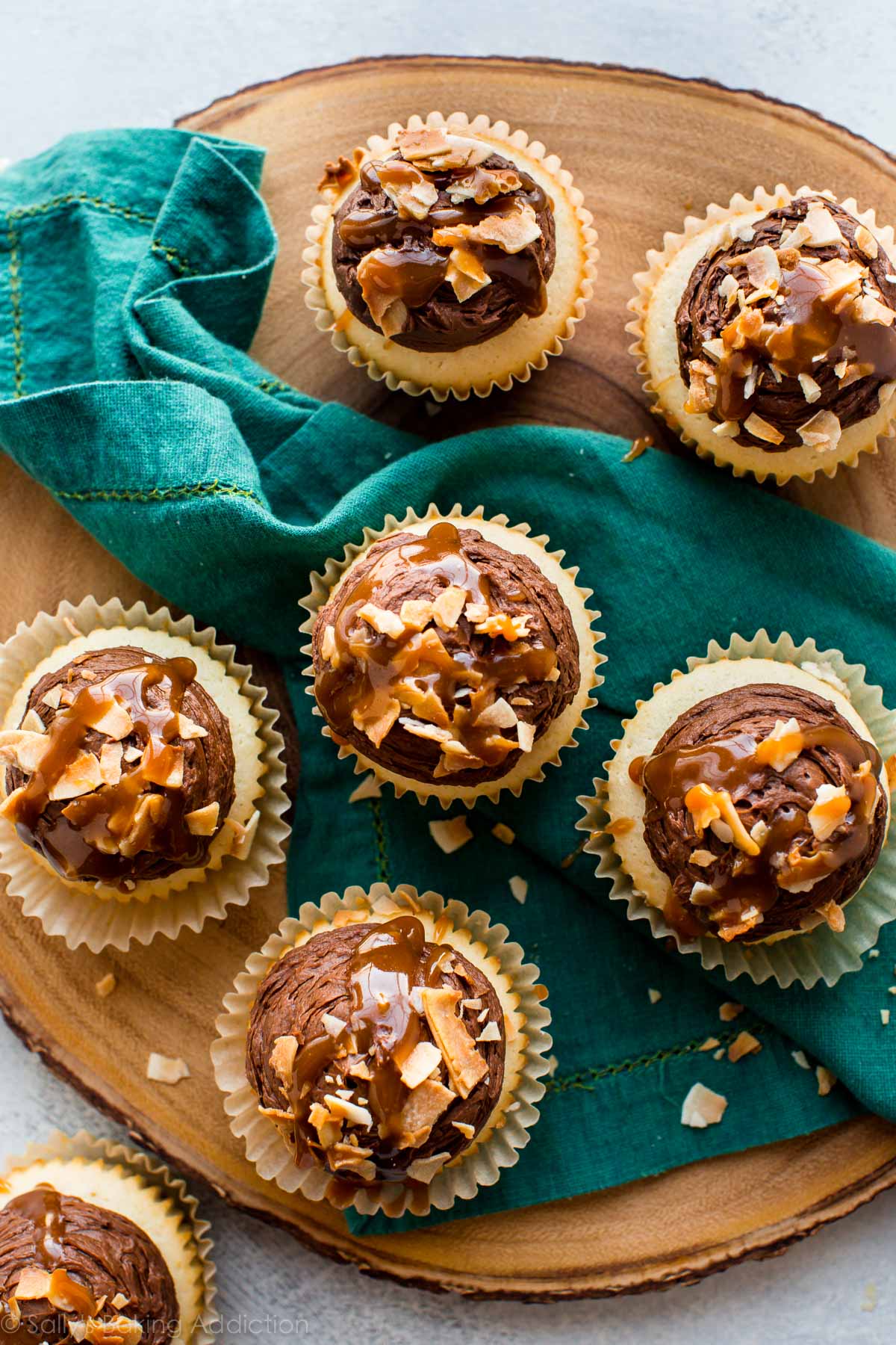 overhead image of chocolate caramel coconut cupcakes on a wood slice serving board