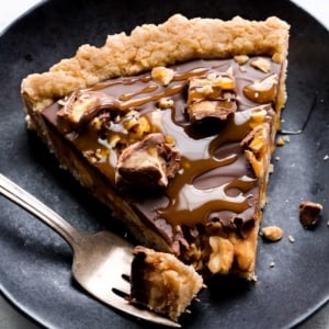 slice of Snickers caramel tart on a black plate with a fork