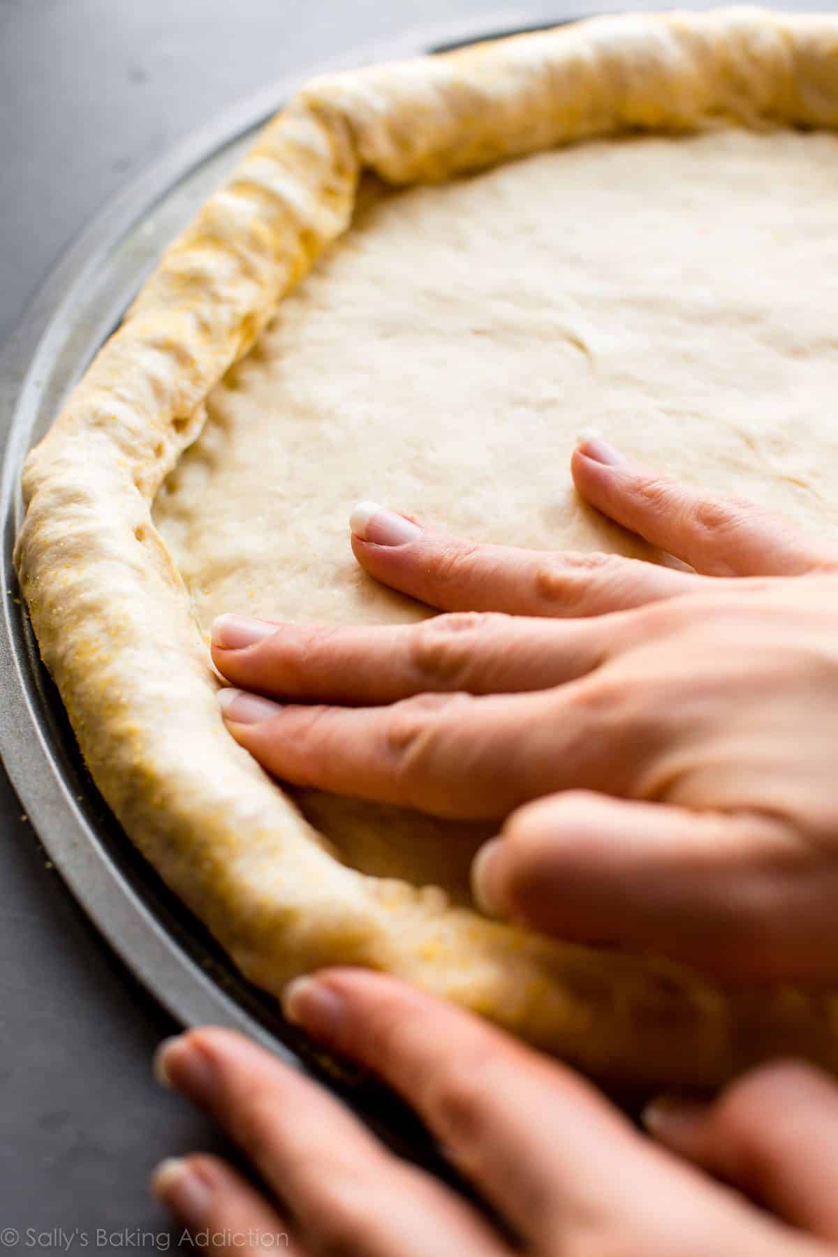 hands folding dough over string cheese for stuffed crust pizza