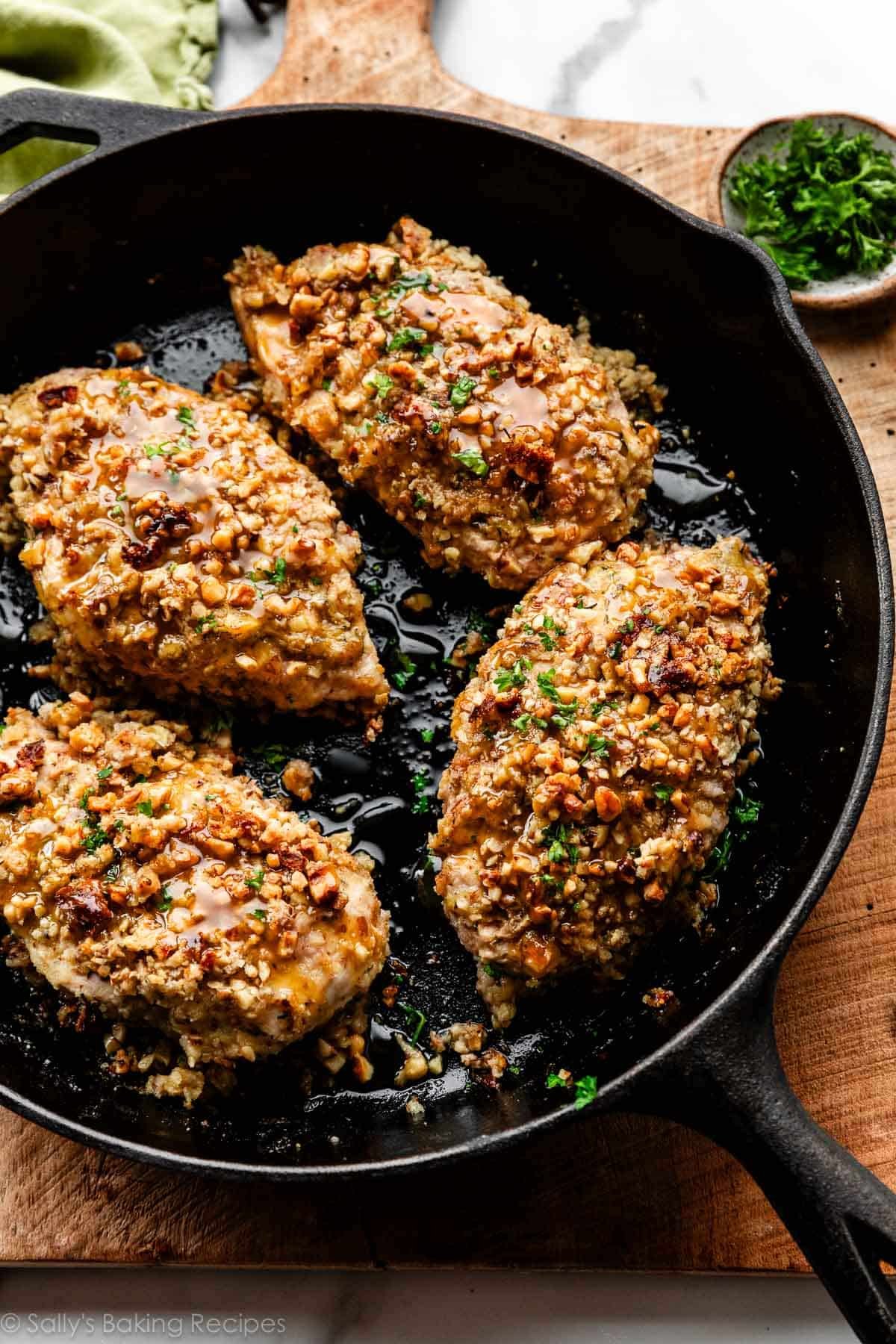 walnut crusted chicken with parsley sprinkled on top in cast iron skillet.