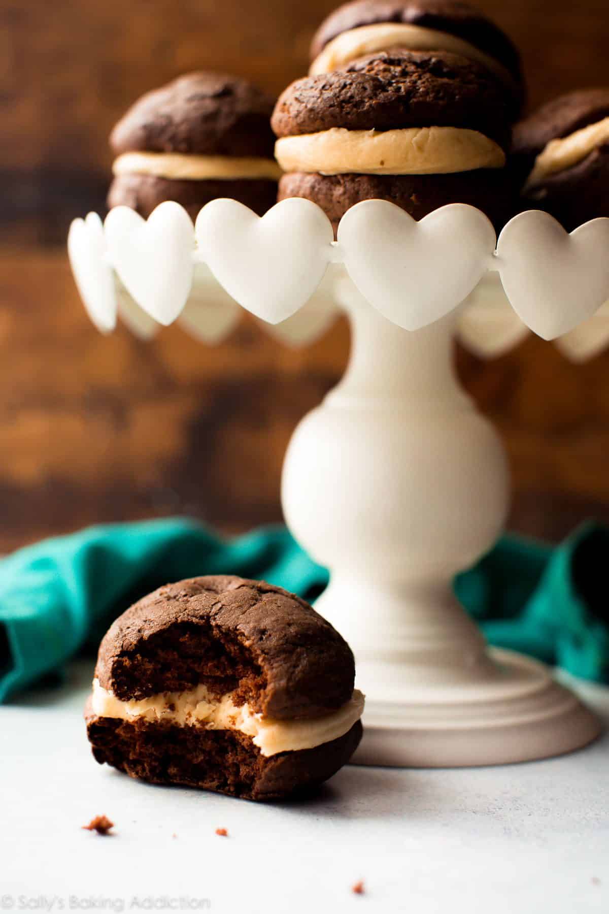 chocolate whoopie pies with salted caramel frosting on a white cake stand and one whoopie pie near the base