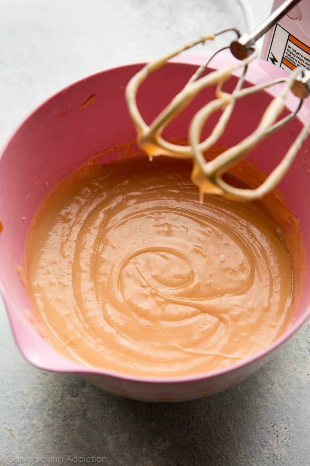 salted caramel frosting in a pink bowl with a hand mixer