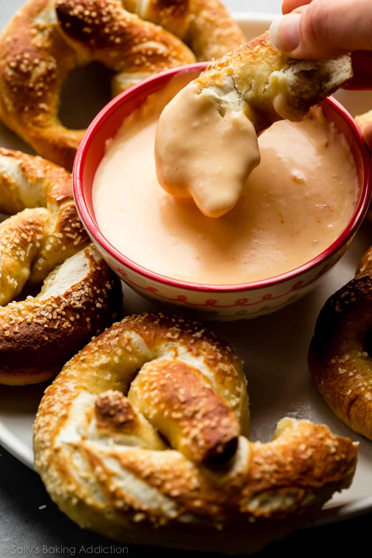 hand dipping piece of soft pretzel into bowl of cheese sauce