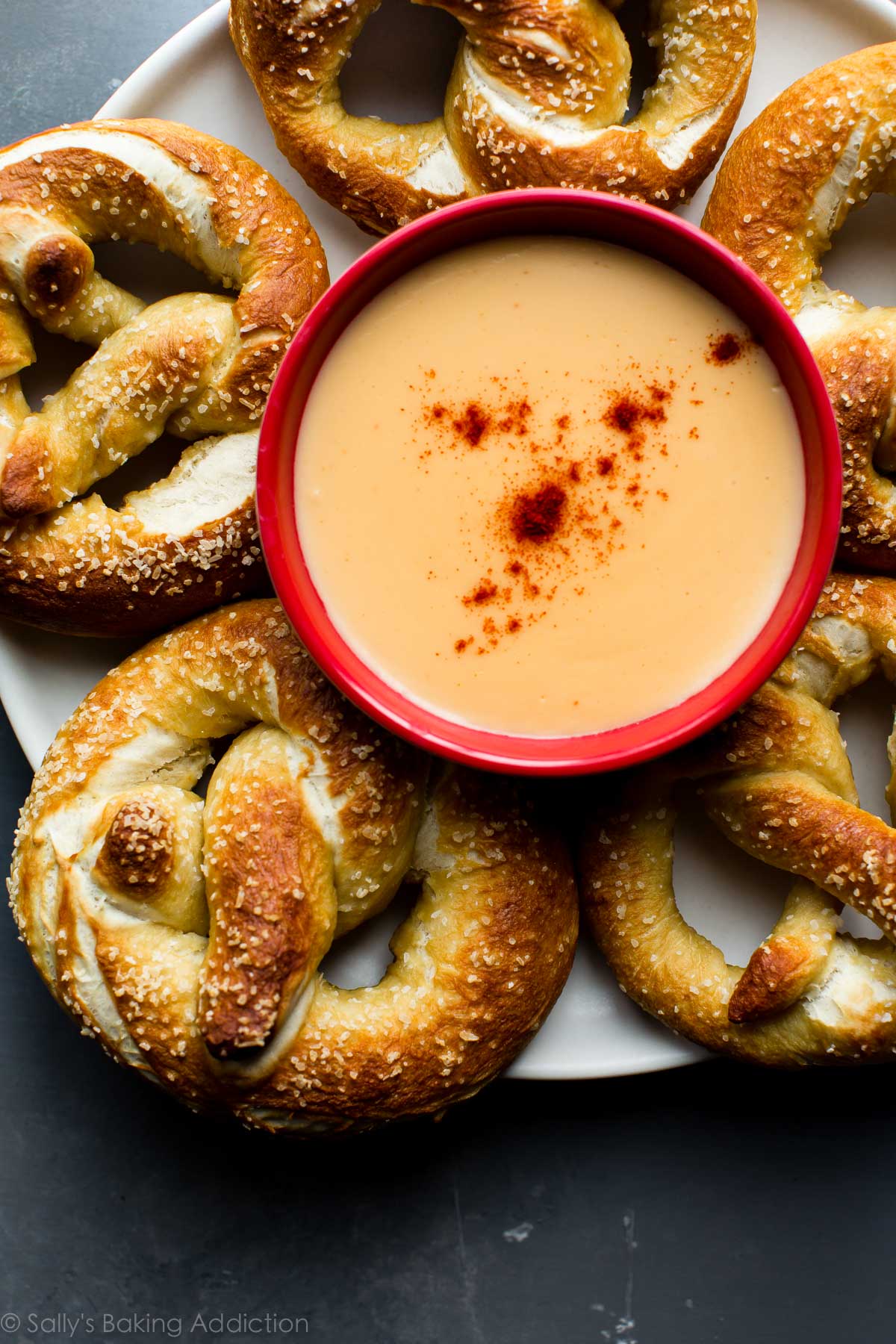 overhead image of soft pretzels on a white plate with a bowl of cheese sauce in the middle