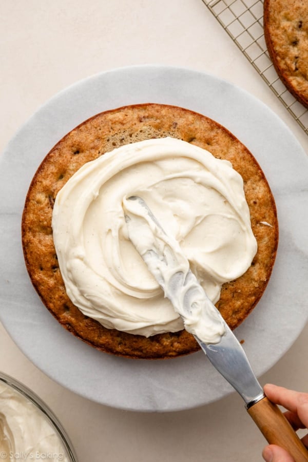 spreading cream cheese frosting on cake.