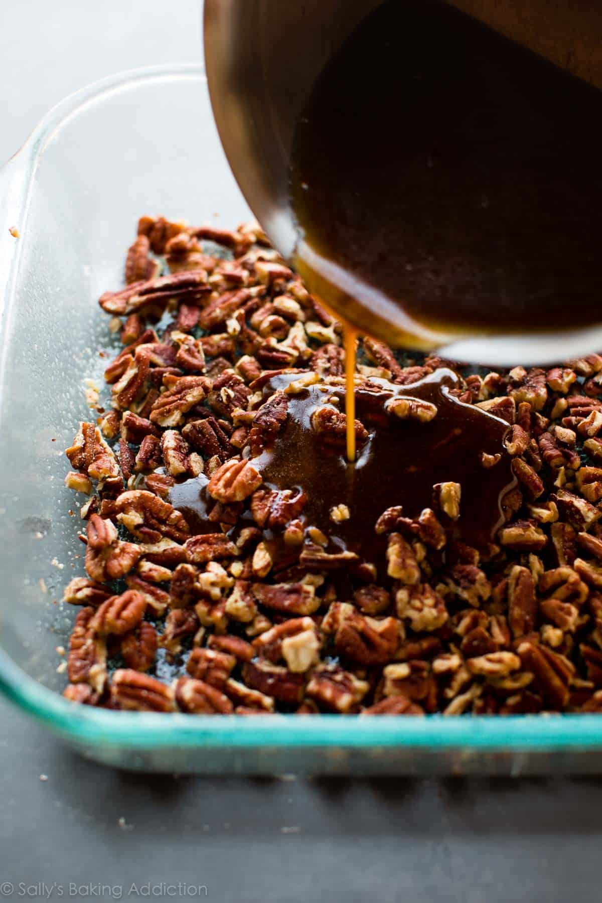 pouring liquid topping ingredients onto layer of pecans in a glass baking dish