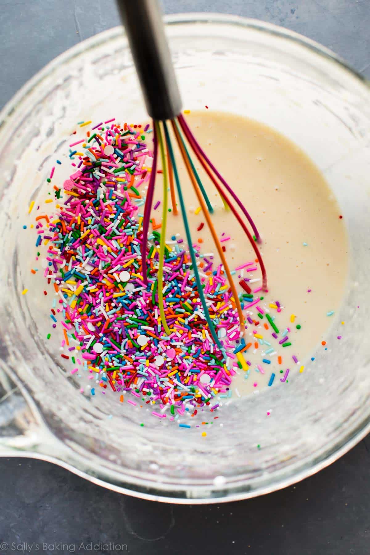 funfetti cupcake batter in a glass bowl with a rainbow colored whisk