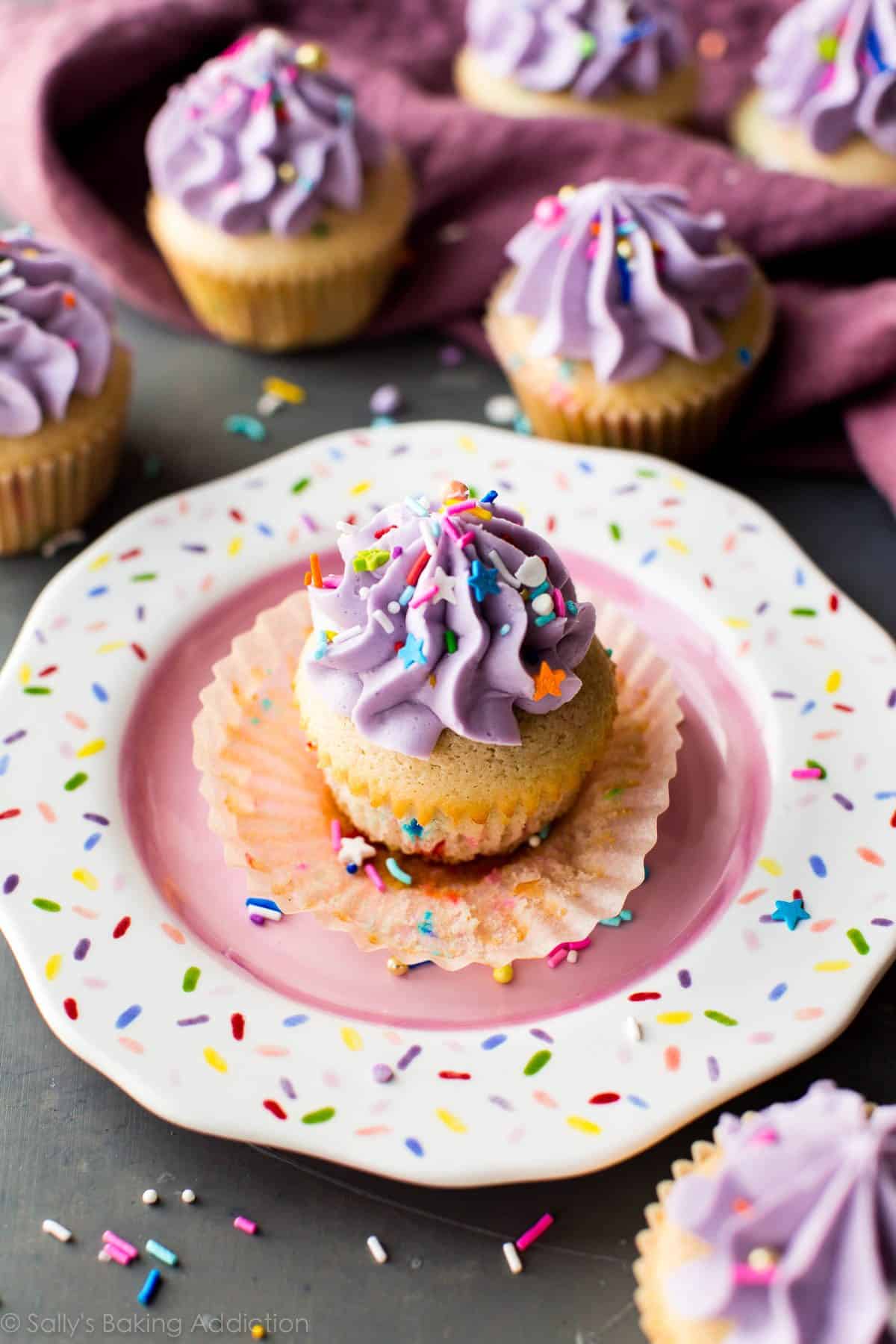 funfetti cupcake with purple frosting and sprinkles on a sprinkle plate