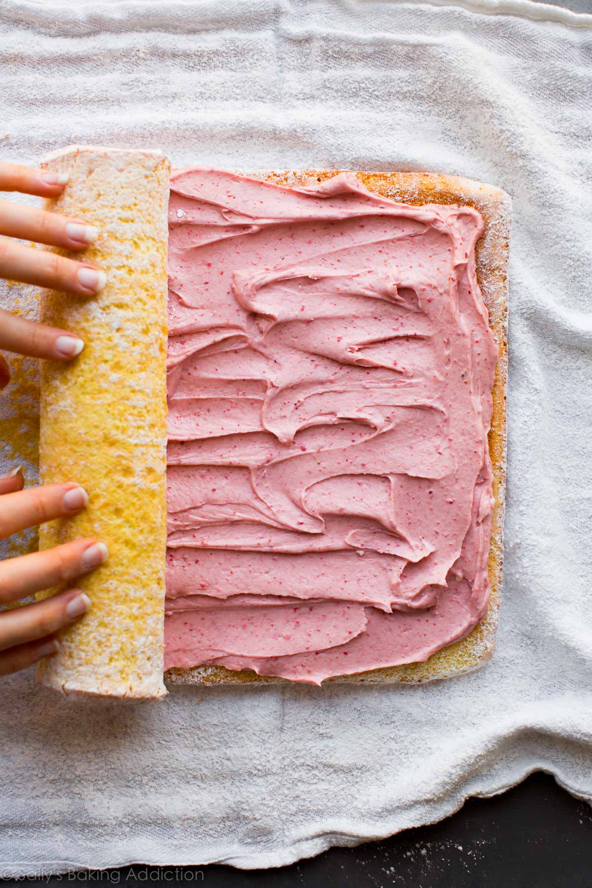 hands rolling up sponge cake with strawberry cream cheese filling