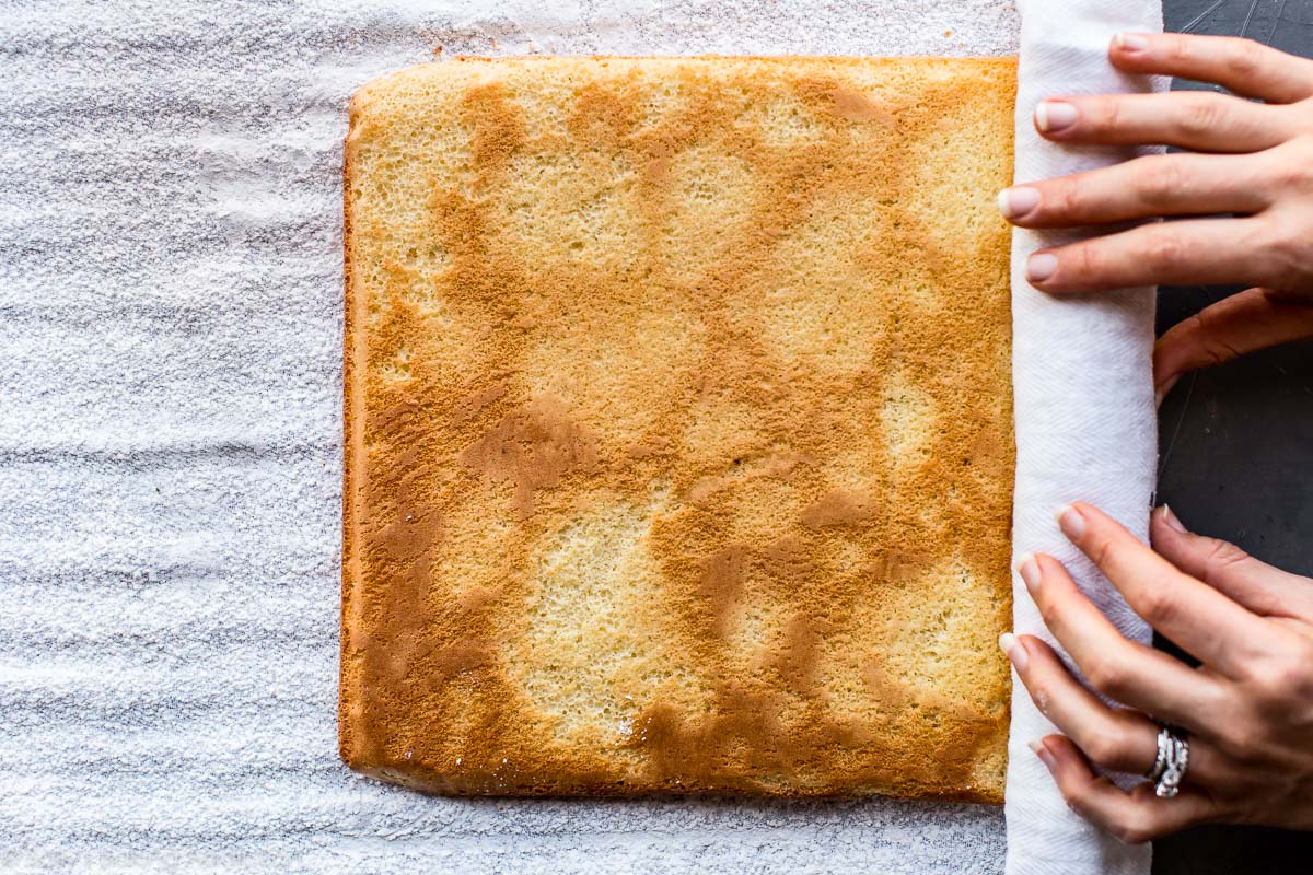 hands rolling up sponge cake in a kitchen towel