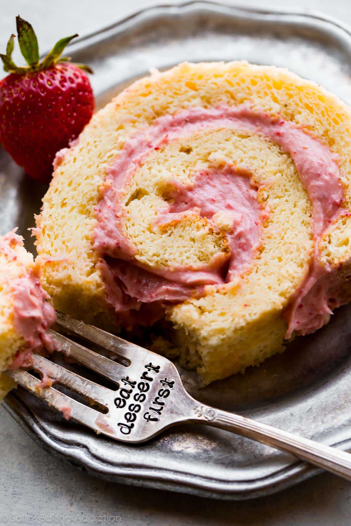 slice of strawberries and cream cake roll on a silver plate with a fork