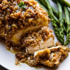 walnut crusted chicken breast on a white plate with asparagus