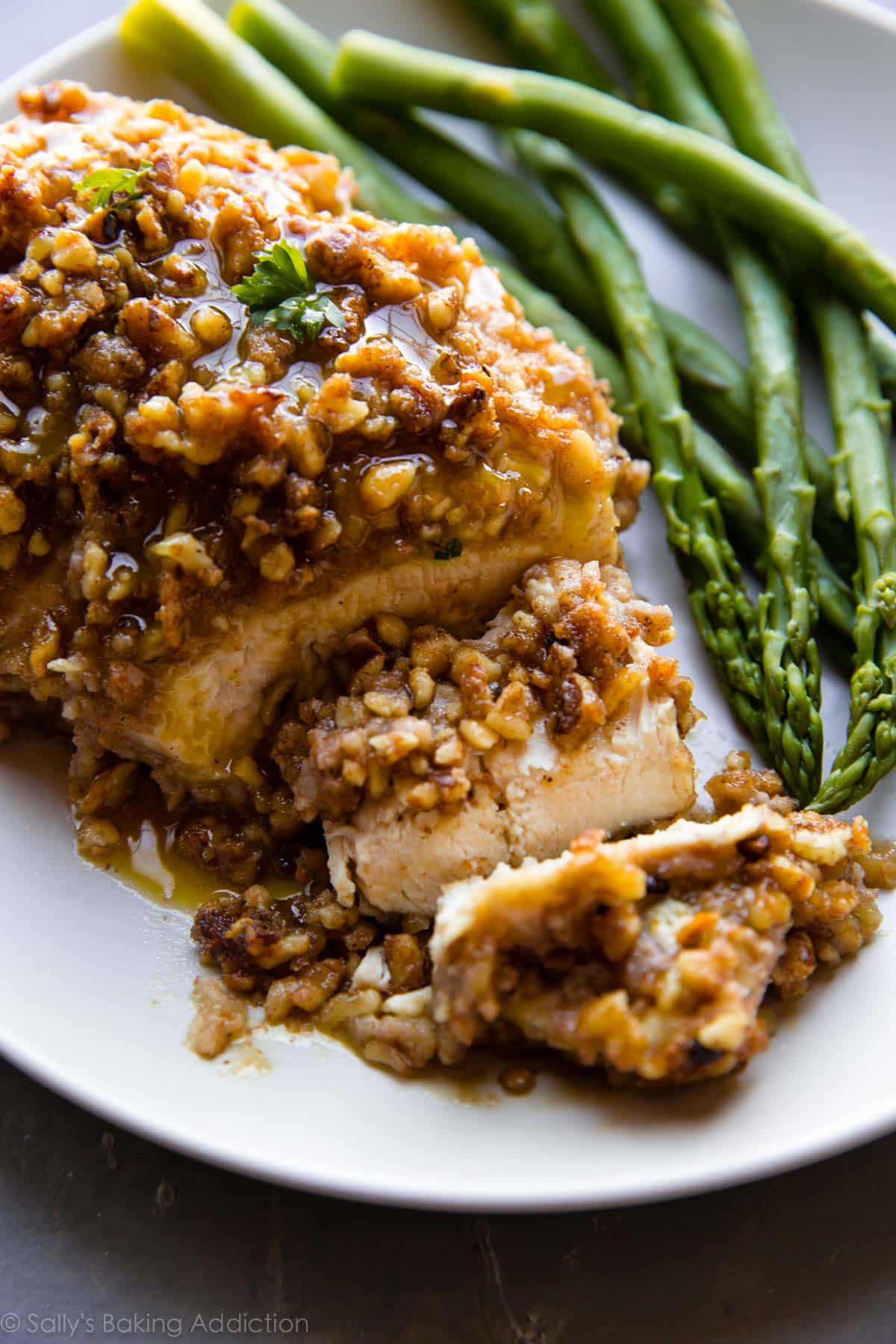 walnut crusted chicken breast on a white plate with asparagus