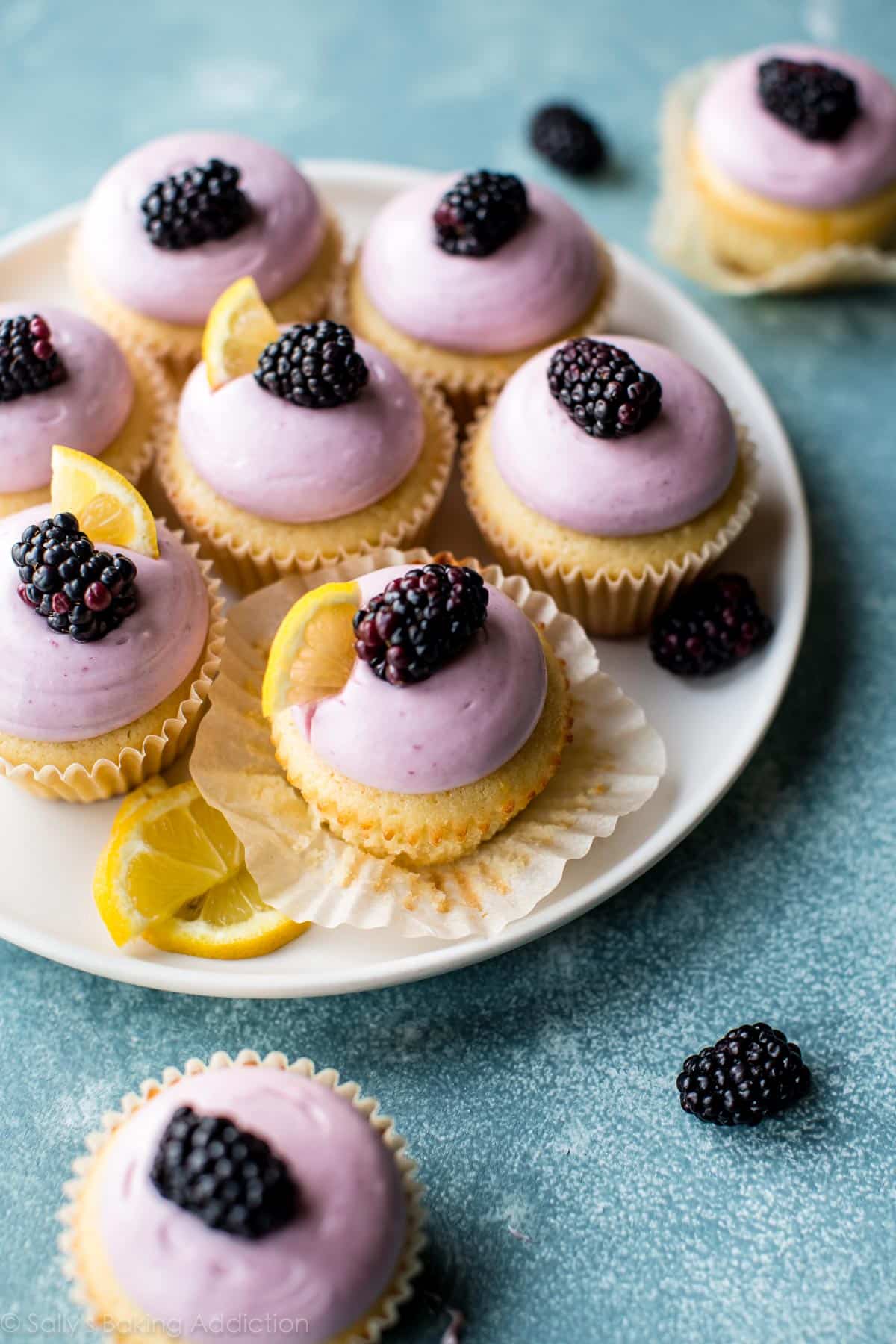 lemon cupcakes with blackberry cream cheese frosting topped with blackberries on a white serving plate