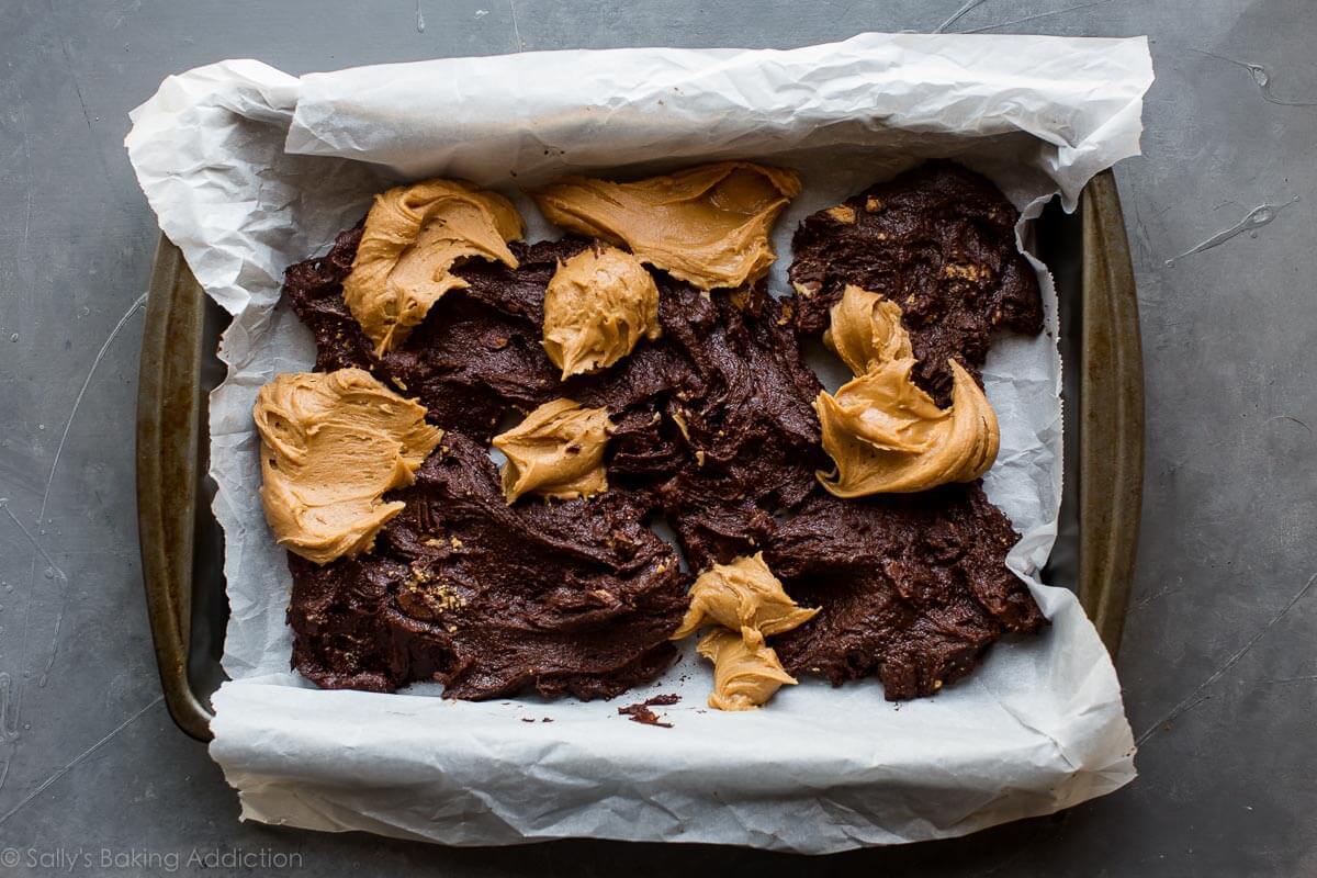 scoops of brownie batter and peanut butter swirl mixture in a baking pan lined with parchment paper