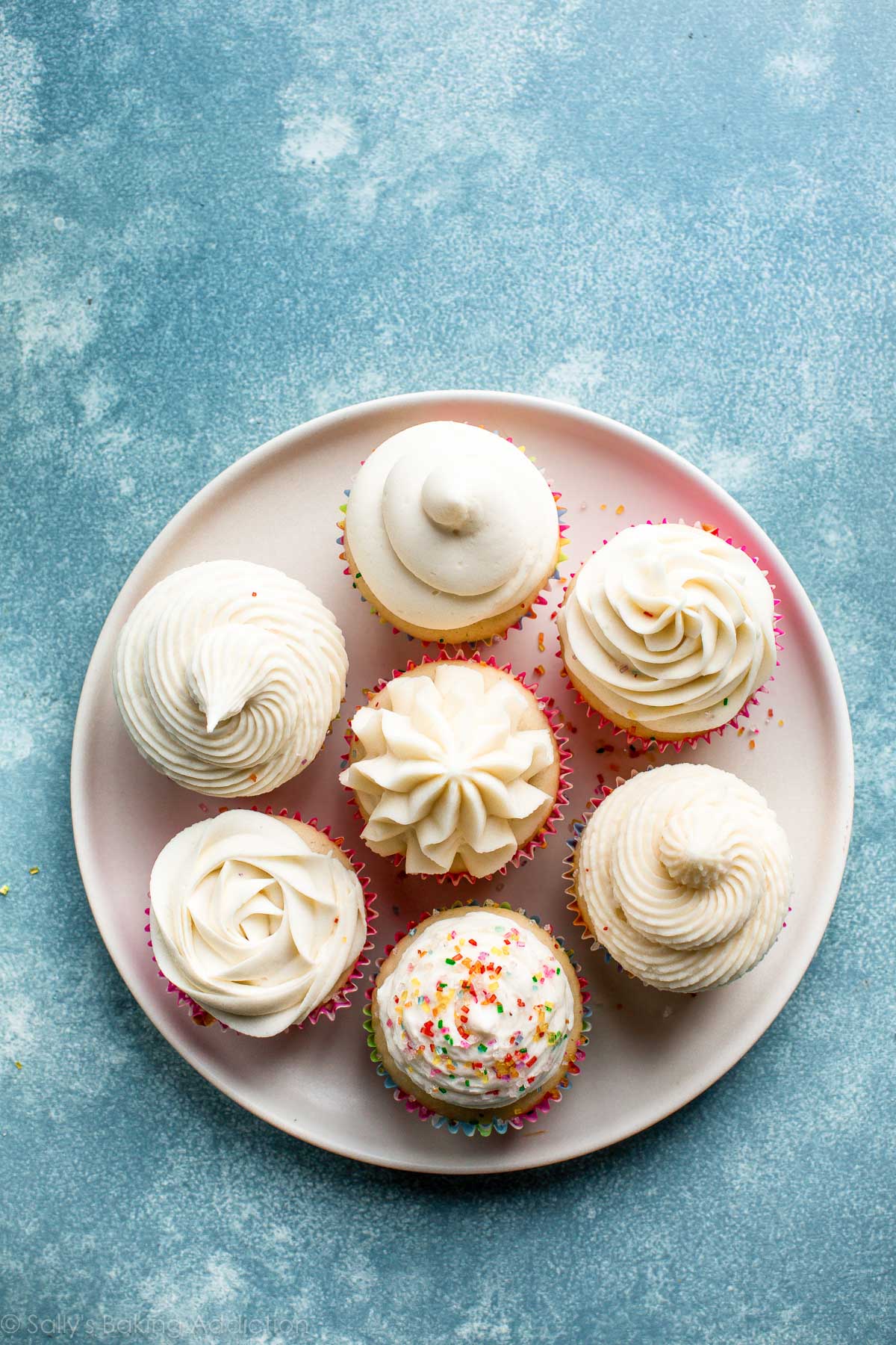 a plate of cupcakes decorated with vanilla buttercream using various piping tips