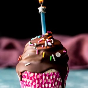 birthday cupcake with chocolate coating and a lit candle