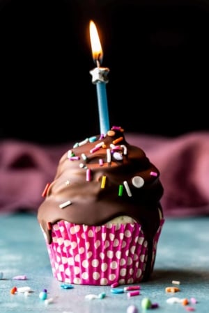 birthday cupcake with chocolate coating and a lit candle