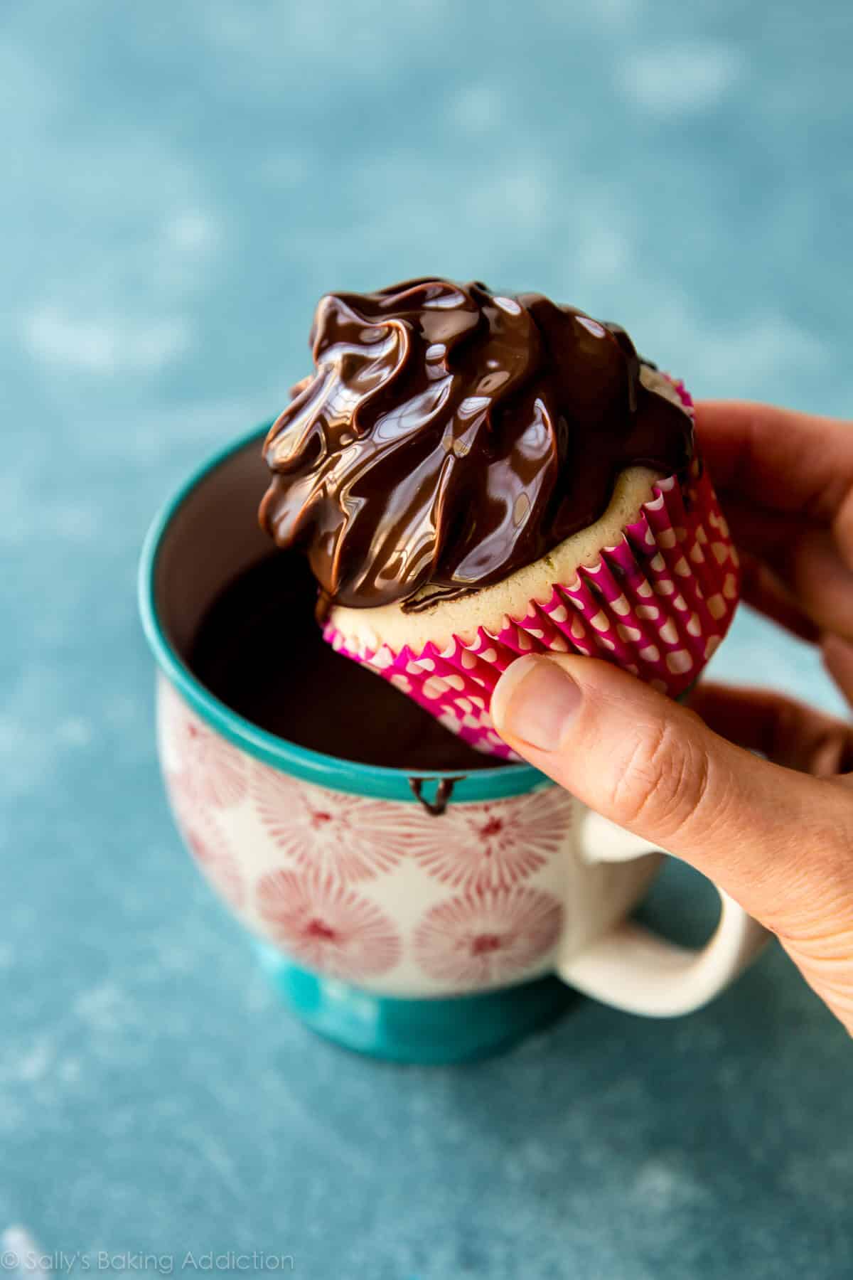 hands dunking cupcake with meringue frosting into chocolate coating