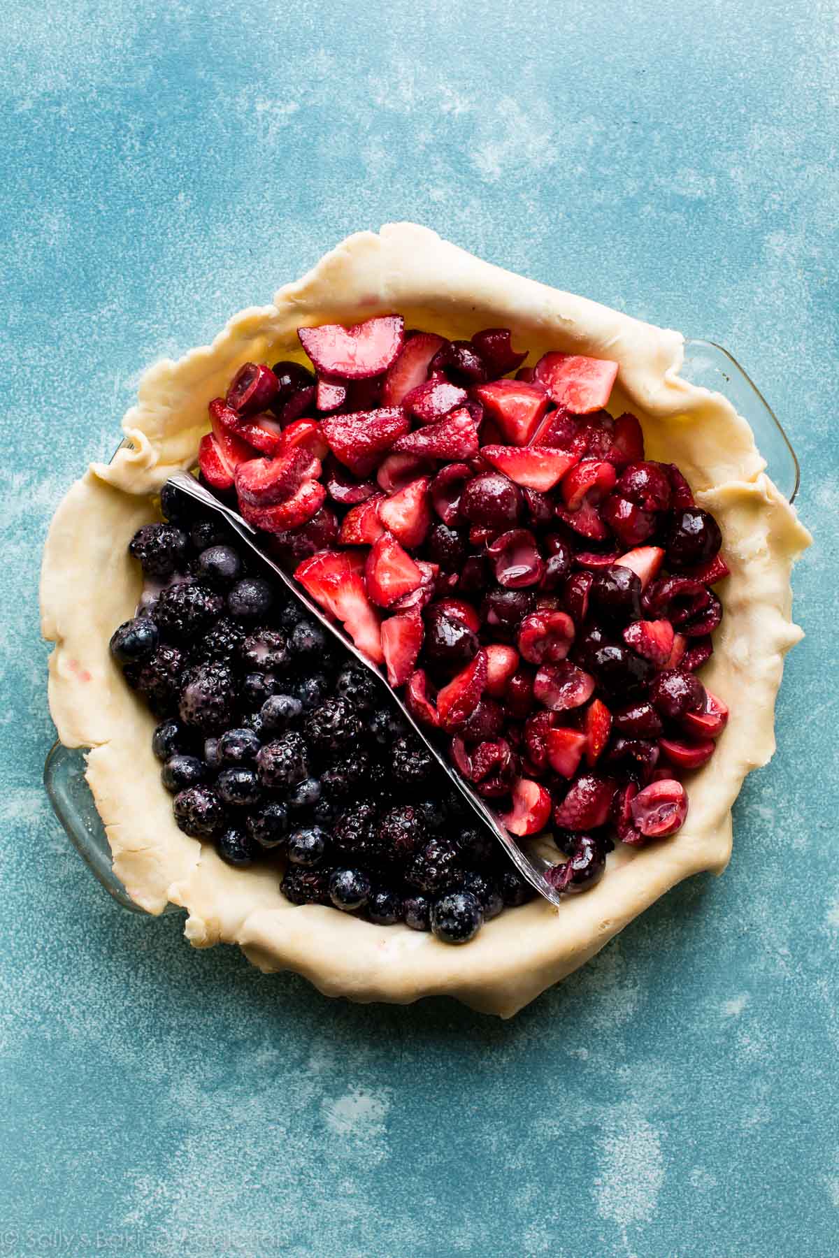 berry filling in pie dish with an aluminum foil divider between the blue and red sections of berries