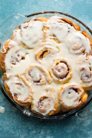 overhead image of orange sweet rolls with orange icing in a glass baking dish