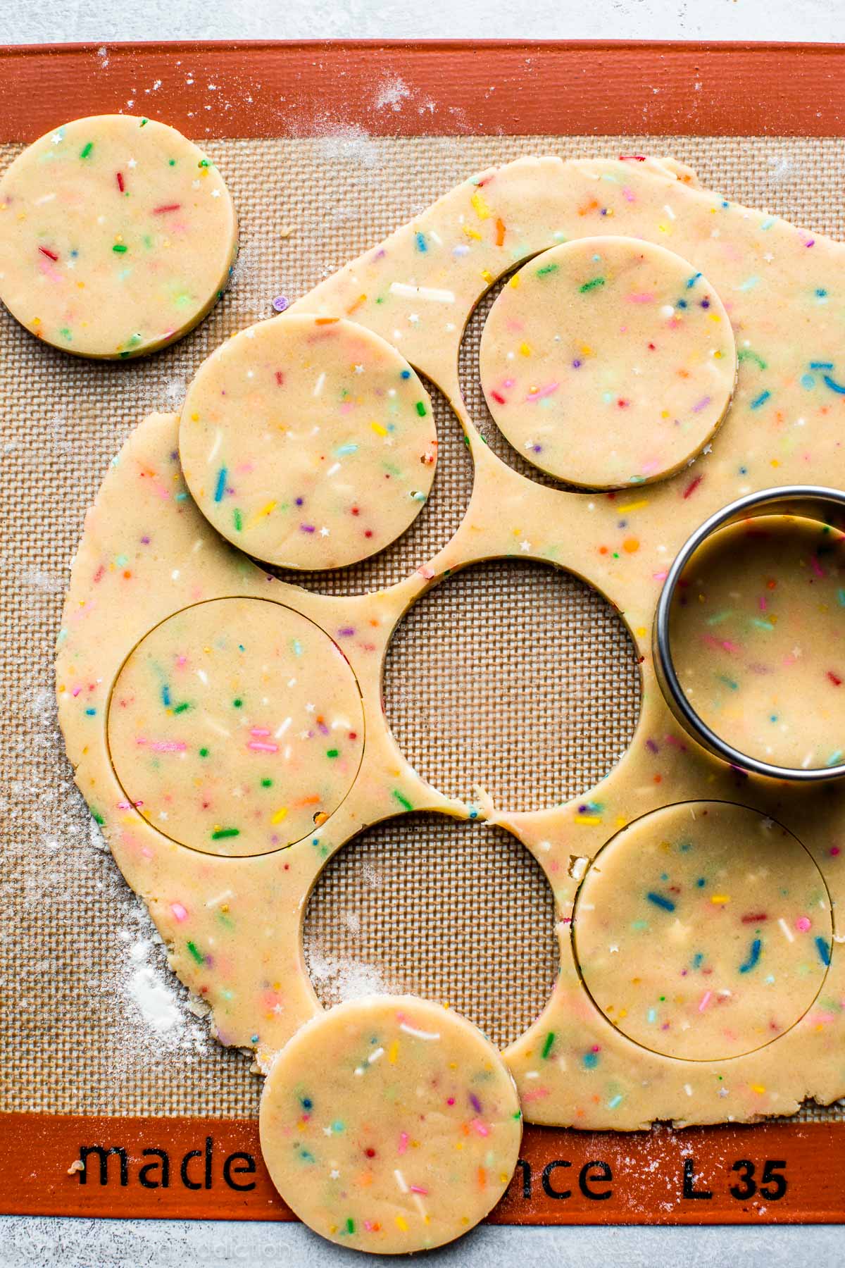rainbow sprinkle cookie dough rolled out on a silpat baking mat with a circle cookie cutter